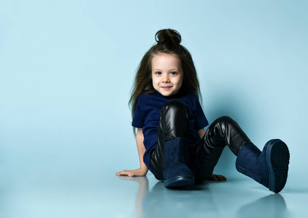 Small smiling girl model with long hair in stylish casual clothing and ugg boots sitting on floor - Photo, Image