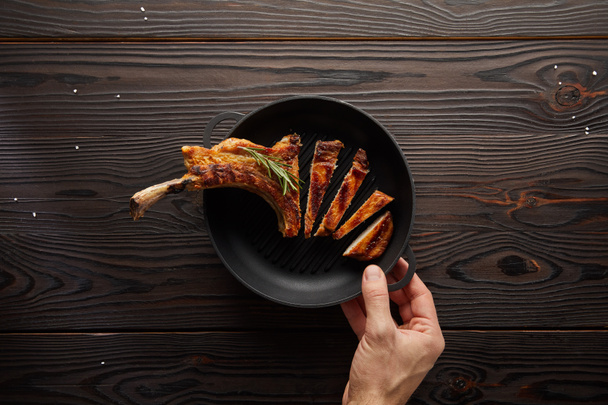 Top view of man holding frying pan with delicious ribeye steak on wooden background - 写真・画像