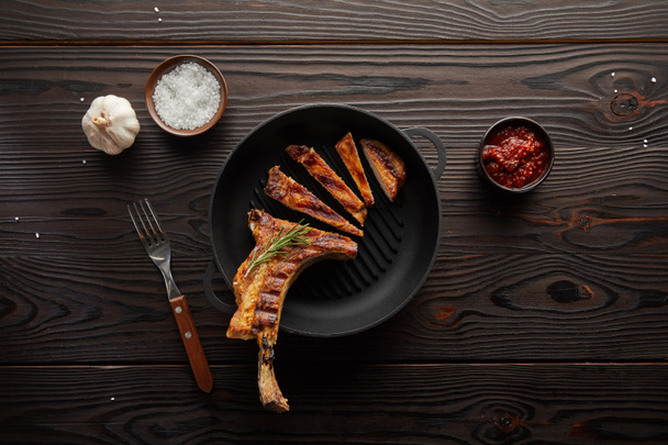 Top view of sliced ribeye steak in frying pan with tomato sauce, garlic and salt on wooden background - 写真・画像
