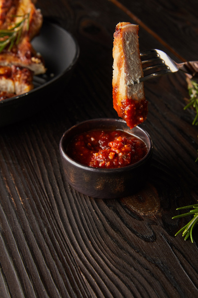 Slice of delicious steak on fork by tomato sauce and rosemary on wooden surface - Photo, Image