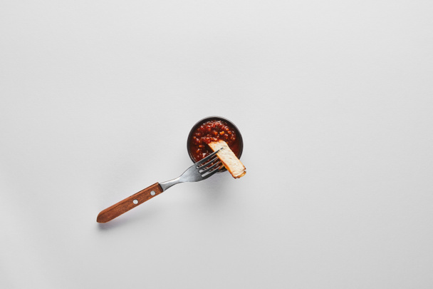 Top view of slice of steak on fork by tomato sauce on white background - Foto, imagen