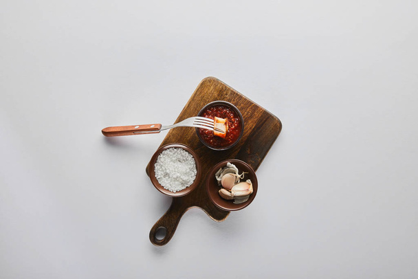 Top näkymä viipale pihvi haarukalla tomaattikastike, valkosipuli ja suola leikkuulauta valkoisella pohjalla
 - Valokuva, kuva