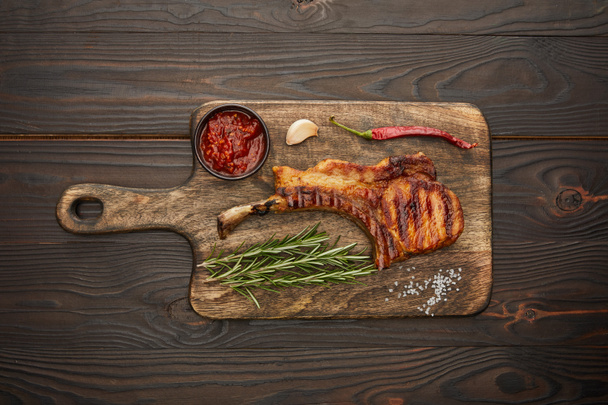 Top view of on gourmet ribeye steak with chili sauce, garlic and rosemary on chopping board on wooden background - Valokuva, kuva