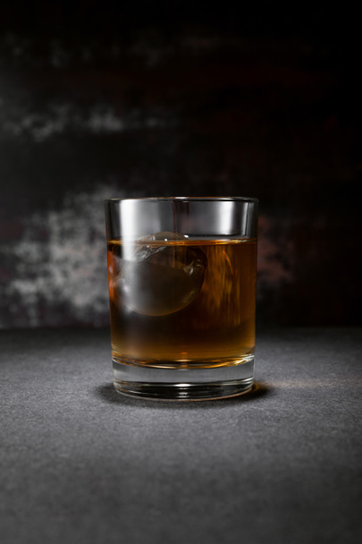 bevroren ijsblokje in glas whisky op zwart met rook - Foto, afbeelding