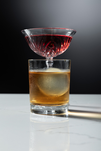 selective focus of ice cube in glass of whiskey near red wine on black  - 写真・画像