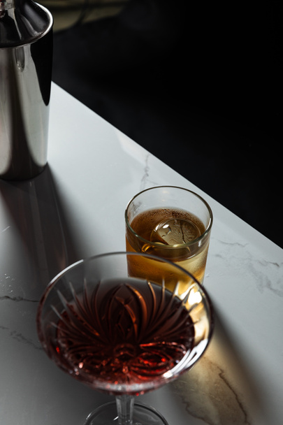 selective focus of glass with whiskey near red wine and shaker isolated on black  - Foto, afbeelding