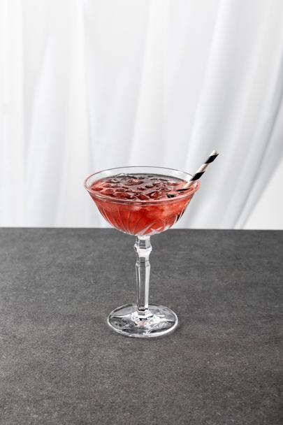 glass with red cosmopolitan cocktail with ice and straw on white  - Fotó, kép