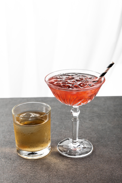 υγρό ποτήρι με ουίσκι κοντά σε κόκκινο κοσμοπολίτικο κοκτέιλ σε λευκό  - Φωτογραφία, εικόνα