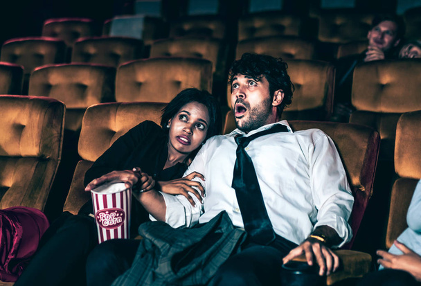 Зрители сидят в кинотеатре и смотрят ужас. Боящаяся женщина, сидящая рядом с мужчиной, шокирована и напугана - Фото, изображение