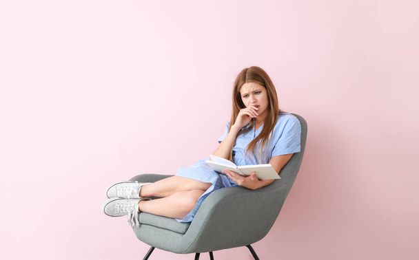 Upset young woman reading book on color background - Фото, зображення