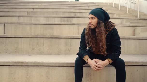 Ritratto di hipster dai capelli lunghi seduto in strada nella città moderna
 - Filmati, video