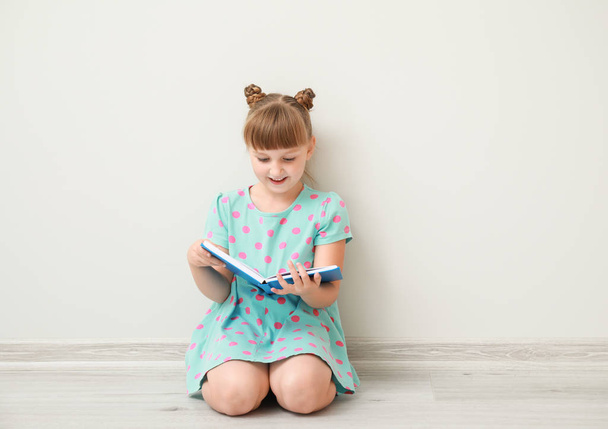 Aranyos kislány könyv ül közel fehér fal - Fotó, kép