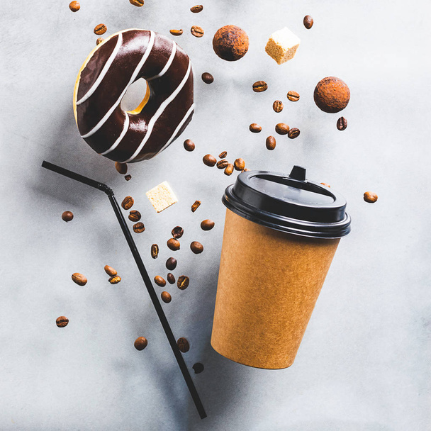 Kahveli kağıt bardak ya da gri arka planda çikolatalı kahve çekirdekli çay çöreği. Yaratıcı modaya uygun yükselme - Fotoğraf, Görsel