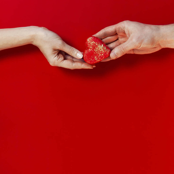 Woman and male hands holding red Heart Shaped Macaroon Cake and confetti on red background topview Flat lay. Creative composition for Valentine's Day love concept birthday present mother day holiday - Foto, Imagem