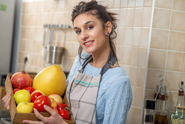 smiling young woman with various fruits in the kitchen - Fotografie, Obrázek