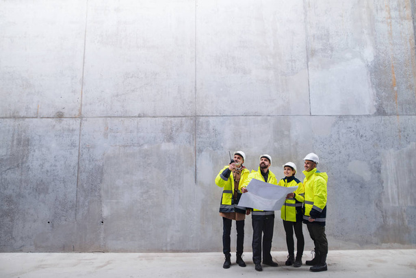 A group of engineers standing against concrete wall on construction site. - 写真・画像