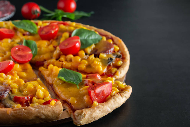 Νόστιμη πίτσα με ντοματίνια και φέτες φέτα σε μαύρο φόντο. Πεντανόστιμη ιταλική πίτσα με τυρί και ντοματίνια σε στρογγυλό ταμπλό, κομμένη σε φέτες τριγωνικό κομμάτι. Αυθεντικό εθνικό πιάτο μεσογειακής κουζίνας. - Φωτογραφία, εικόνα