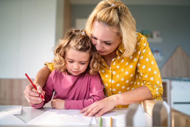 A cute small girl with mother indoors at home, drawing pictures. - Foto, Imagem