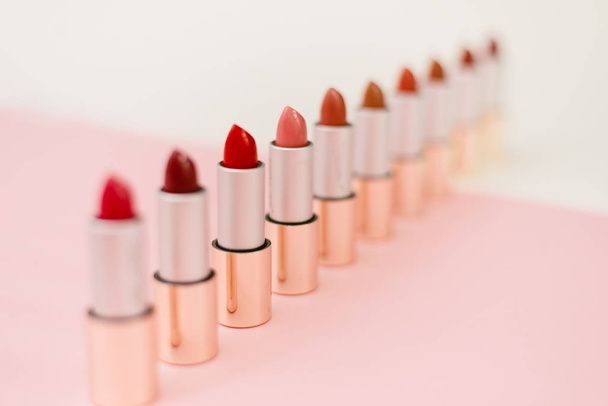 a lot of different lipsticks stand on a beige and pink background. Pattern and concept of beauty, cosmetics, women's accessories. Shades of lipstick tubes - Photo, Image