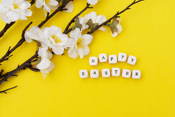 Happy Easter. Cubes with text on yellow background. Spring brunches with white flowers. Minimalistic flat lay. - Photo, image