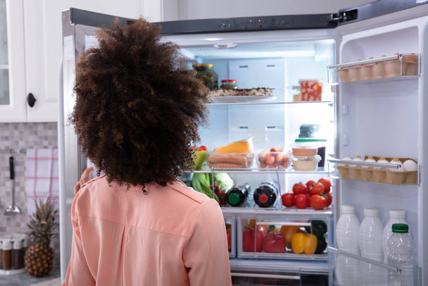 Rear View Of A Confused Woman Searching For Food In An Open Refrigerator - Fotó, kép