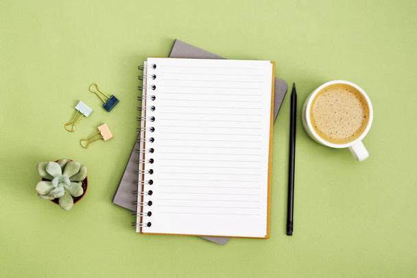 Open notebook with empty page and coffee cup. Table top, work space on green background. Creative flat lay. - Fotografie, Obrázek