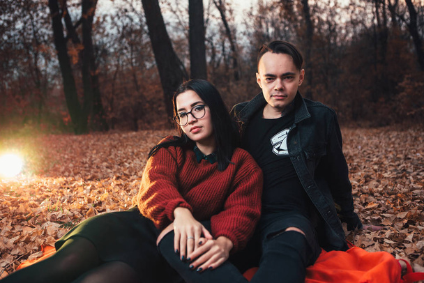young man and young woman are sitting on a plaid in an autumn forest. - Φωτογραφία, εικόνα