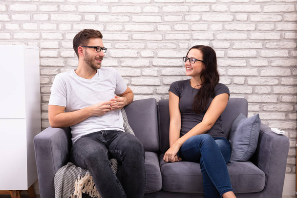 Young Men And Woman Sitting On Sofa Looking At Each Other During Date - Photo, Image