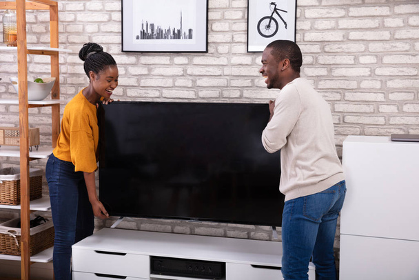 Side View Of Young African Couple Lifting Television At Home - Fotó, kép