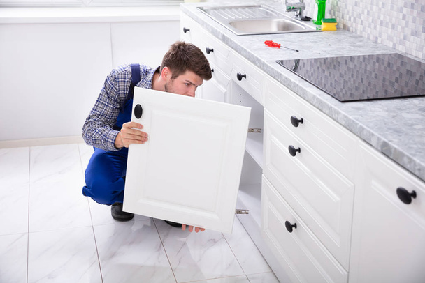 Crouching Repairman Fixing The Door Of Kitchen Sink - Фото, зображення