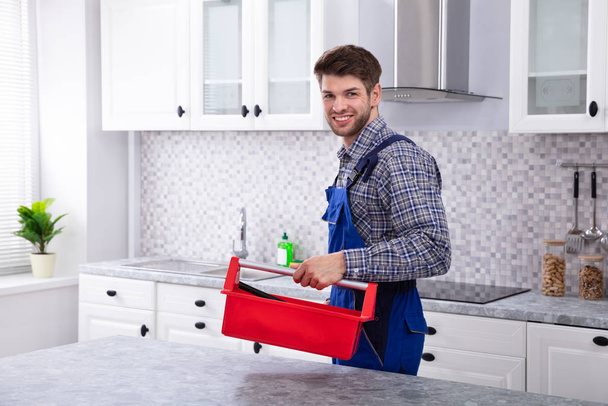 Szczęśliwy mężczyzna naprawy z Red Toolbox stoi w kuchni - Zdjęcie, obraz