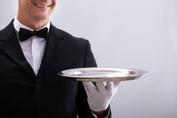 Close-up Of Waiter's Hand Holding Empty Silver Tray Against White Background - Фото, изображение