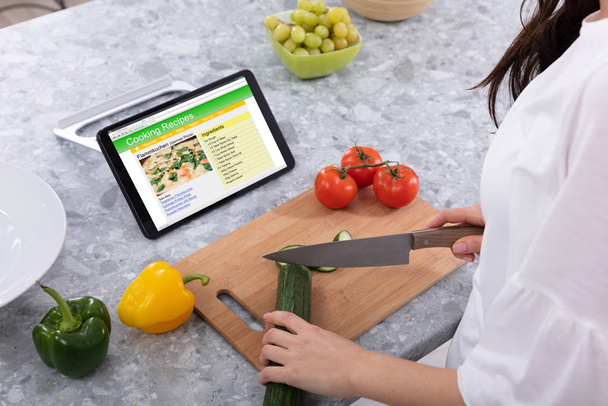 Woman Cutting Cucumber With Kitchen Knife Near Cooking Recipes On Digital Tablet Screen - Photo, Image