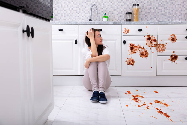 Szomorú nő ül a padló a konyhában kiömlött élelmiszer - Fotó, kép