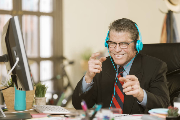 Professional man in a creative office listening to headphones and making a silly gesture - Fotoğraf, Görsel
