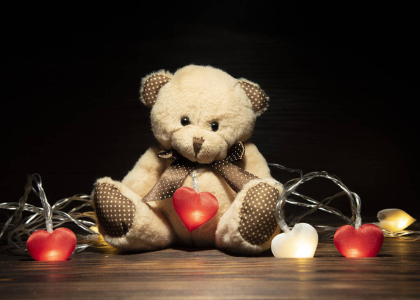 Soft toy bear and garland with hearts on a dark background. - Φωτογραφία, εικόνα