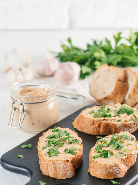 Close up view of slice bread with homemade turkey pate and fresh green parsley on black kutting board over white concrete background, Copy space. - Foto, Bild