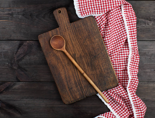 Empty very old wooden kitchen cutting board and a red towel on a brown table, the view from the top - Фото, изображение