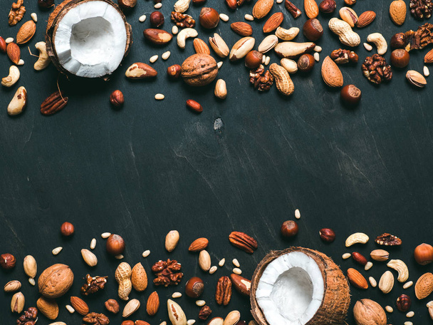 Background of mixed nuts - coconut, hazelnuts, walnuts, almonds, pecan, pistachio, brazil nut, pine nuts, peanut - on dark background. Copy space. Top view or flat lay - Zdjęcie, obraz