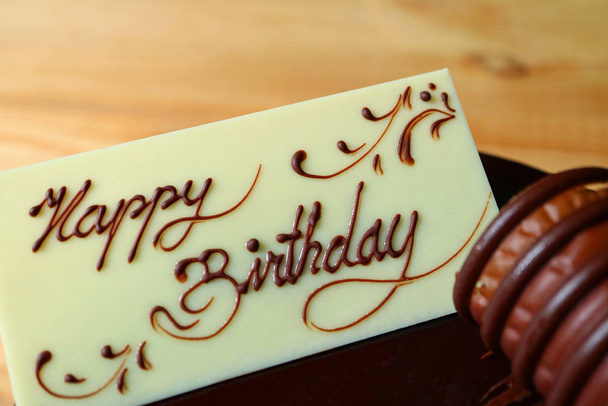 Nahaufnahme eines Glückwunsches zum Geburtstag, geschrieben auf der Karte aus weißer Schokolade, gekrönt auf Schokolade-Geburtstagstorte - Foto, Bild