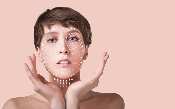 The lifting, skin, plastic surgery concept. Woman face with marks and arrows. Portrait of young caucasian woman at studio isolated on pastel. Short haircut, long neck, perfect skin. Lifting by gold thread concept - 写真・画像