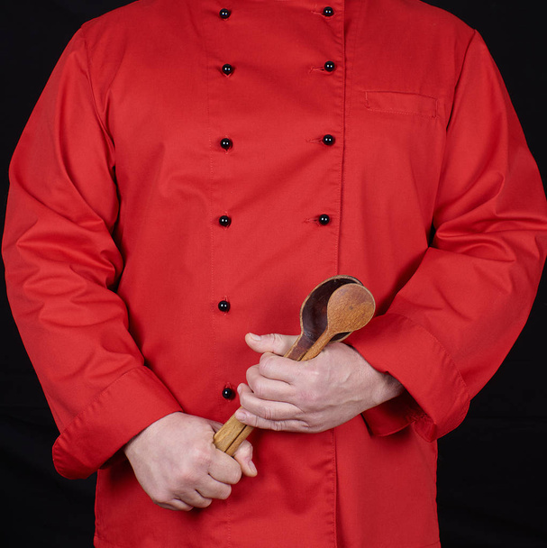 chef in red uniform holding old wooden spoons, black background - Fotó, kép