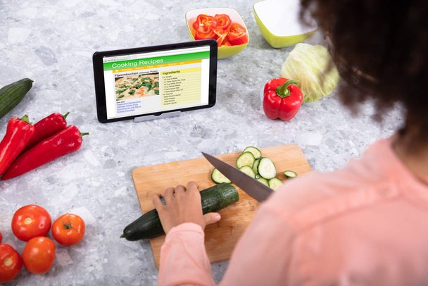 Γυναικείο χέρι κοπής λάχανο στον πίνακα κοπής με συνταγές μαγειρικής σε ψηφιακή οθόνη tablet - Φωτογραφία, εικόνα
