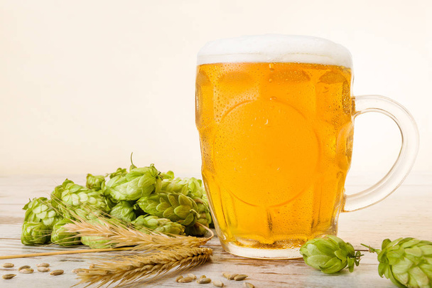 Glass of cold beer with water drops, hops and barley on wooden table. - Photo, Image