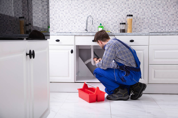 Male Plumber Besides Red Toolbox Fixing Sink In Kitchen - Fotó, kép