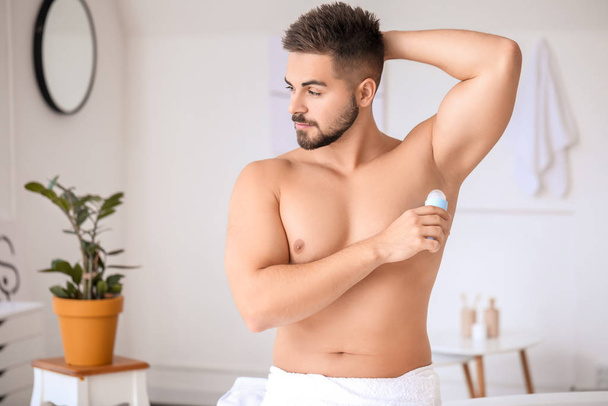 Handsome young man using deodorant in bathroom - Foto, Imagem
