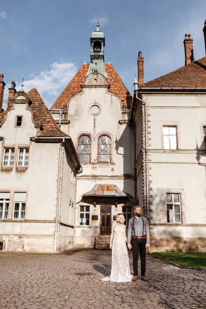 Beautiful wedding couple are walking near old castle, ancient restored architecture, old building, old house outside, vintage palace outdoor. Romantic love in vintage atmosphere street - Zdjęcie, obraz