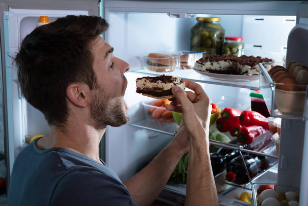 Portrait Of A Happy Man Eating Cake Near Open Refrigerator - Fotoğraf, Görsel
