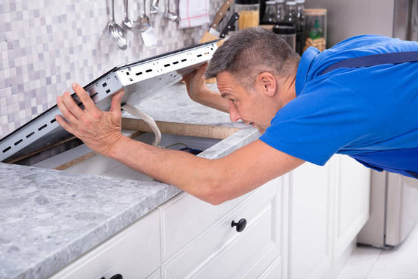 Mature Repairman Installing Induction Stove In Kitchen - Foto, imagen