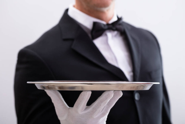 Close-up Of Waiter's Hand Holding Empty Silver Tray Against White Background - Foto, afbeelding